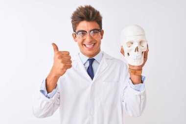 Gözlüklü yakışıklı doktor beyaz arka planda kafatası tutuyor. Kocaman gülümsüyor. Tamam işareti yapıyor.