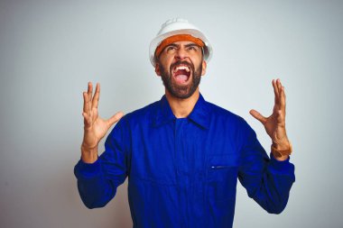 Üniformalı ve kasklı yakışıklı Hintli işçi izole edilmiş beyaz arka planda deli deli deli bağırıyor ve agresif bir ifade ve kollarla bağırıyor. Hayal kırıklığı konsepti.