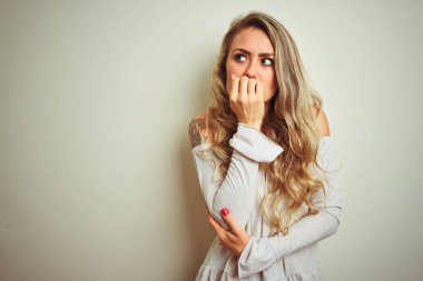 İzole edilmiş beyaz arka planda duran genç ve güzel bir kadın gergin görünüyor ve elleri ağızdan tırnak yiyor. Endişe sorunu.