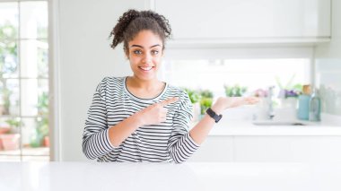 Afro saçlı, güzel Afro-Amerikalı kadın. Sıradan çizgili süveter giyiyor. Kameraya hayret ediyor ve gülümsüyor..