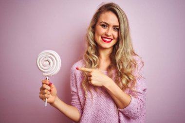 Genç güzel kadın pembe izole arka plan üzerinde tatlı şeker yeme çok mutlu el ve parmak ile işaret