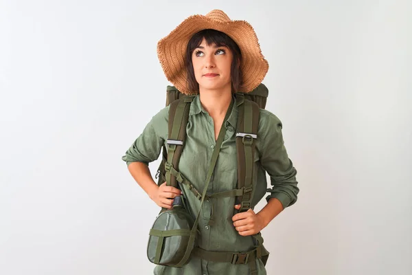 Hiker woman wearing backpack hat and water canteen over isolated white background smiling looking to the side and staring away thinking.