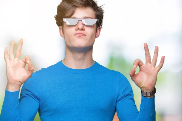 Young man wearing funny thug life glasses over isolated background relax and smiling with eyes closed doing meditation gesture with fingers. Yoga concept.