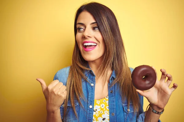 Young Beautiful Woman Eating Chocolate Donut Yellow Background Pointing Showing — Stok fotoğraf