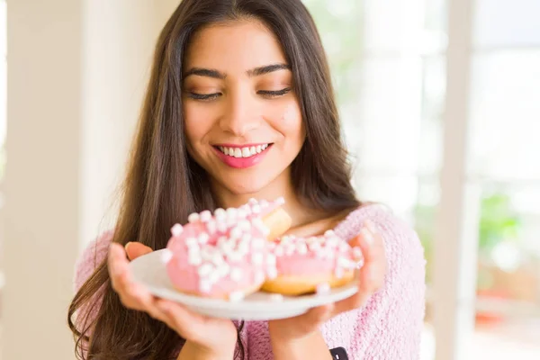 おいしいピンクのドーナツでいっぱいの皿を抱えた美しい若い女性 — ストック写真