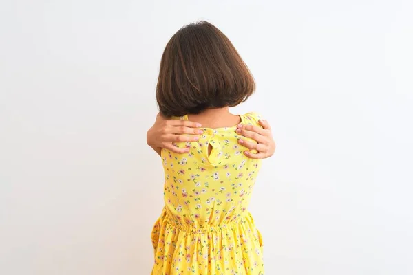 年轻美丽的小女孩穿着黄色的花衣 站在孤零零的白色背景上 欢快地拥抱着自己 从后面又是积极的 自爱和自我照顾 — 图库照片