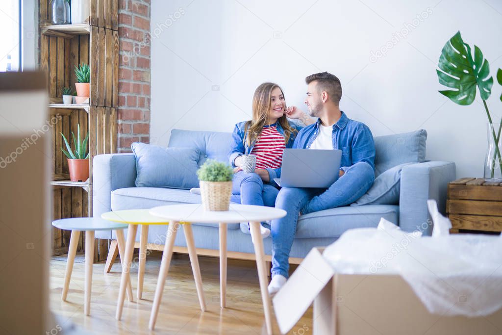 Young couple relaxing sitting on the sofa using the computer laptop around cardboard boxes, very happy moving to a new house