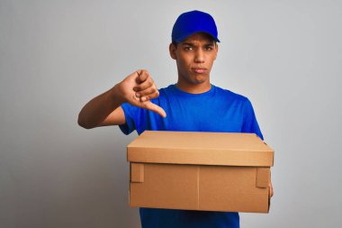 Genç yakışıklı Arap teslimatçı, izole edilmiş beyaz arka planda duran, kızgın yüzlü, olumsuz işaretli, başparmakları aşağıda, reddedilme kavramından hoşlanmayan bir kutu tutuyor.