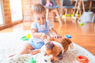 Güzel çocuk, anaokulunda battaniyeye oturmuş oyuncak köpekle oynuyor.