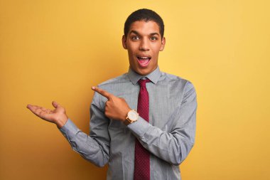 Genç yakışıklı Arap işadamı gömlek ve kravat giyerek izole edilmiş sarı arkaplanı hayranlıkla izliyor ve kameraya gülümsüyor..
