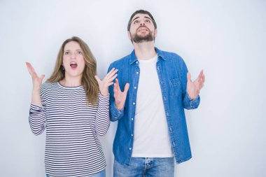 Genç güzel çift birlikte beyaz izole arka plan deli ve deli bağırarak ve agresif ifade ve kollar kaldırdı ile bağırıyor üzerinde ayakta. Hayal kırıklığı kavramı.