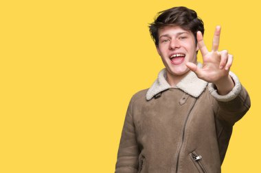 Gösterilen arka plan üzerinde kış ceket giyen genç yakışıklı adam izole ve parmakları ile işaret kendinden emin ve mutlu gülümseyerek iken üçüncü.