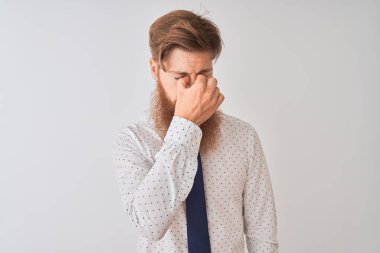 Genç kızıl saçlı İrlandalı işadamı, izole edilmiş beyaz arka planda duruyor. Burnu ve gözleri ovuşturup yorgun ve baş ağrısı çekiyor. Stres ve hüsran kavramı.