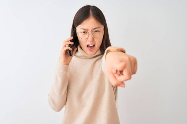 Akıllı telefondan konuşan Çinli genç bir kadın izole edilmiş beyaz arka planda kameraya kızgın ve sinirli olduğunu gösteriyor.