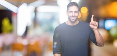 Ve kendinden emin ve mutlu gülümseyerek süre parmak numaralı yukarıyı gösteren izole arka plan üzerinde kazak giyen genç yakışıklı adam.