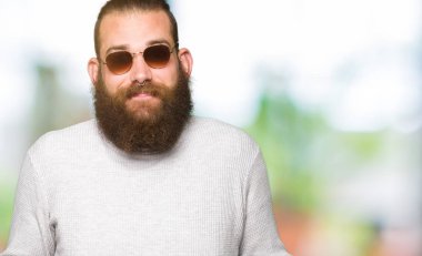 Güneş gözlüğü clueless ve şaşkın bir ifadeyle kollar ve eller kaldırdı giyen genç hipster adam. Şüphe kavramı.