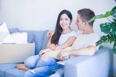 Karton kutuların etrafındaki yeni evdeki kanepede oturan genç ve güzel çift.