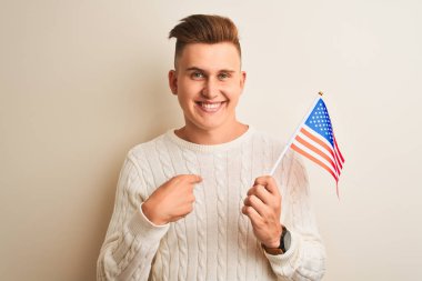 Genç yakışıklı adam izole edilmiş beyaz arka planda Usa bayrağı taşıyor. Şaşırmış yüz ifadesi kendini işaret ediyor.