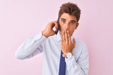 Akıllı telefondan konuşan genç yakışıklı iş adamı pembe arka plan üstü kapalı ağız hata yüzünden utançla, korkunun ifadesi, sessizlikten korkmak, gizli konsept.