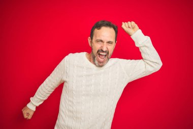 Yakışıklı, orta yaşlı, gri saçlı, soyutlanmış, kırmızı arka planda dans eden mutlu ve neşeli, hareketli, rahat ve kendinden emin, müzik dinleyen bir adam.