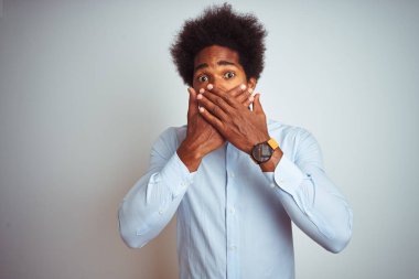 Afro saçlı, yalıtılmış beyaz arka planda zarif bir gömlek giyen Afro-Amerikalı genç bir adam ağzını yanlışlıkla elleriyle kapatarak şok etti. Gizli konsept.