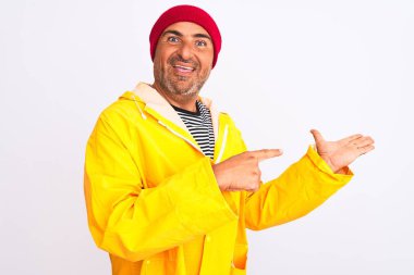 İzole edilmiş beyaz arka planda duran yünlü şapkalı ve yağmurluk giyen orta yaşlı adam kameraya hayret ediyor ve gülümsüyor..