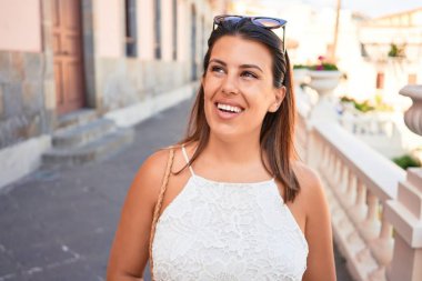 Genç ve güzel bir kadın mutlu bir şekilde gülümsüyor güneşli bir yaz gününde şehir sokaklarında yürüyor.