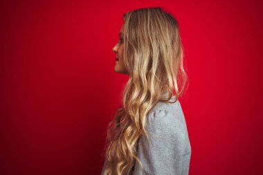 Zarif bir ceket giyen genç ve güzel bir iş kadını. Kırmızı izole edilmiş arka planda duruyor. Yan tarafa bakıyor..