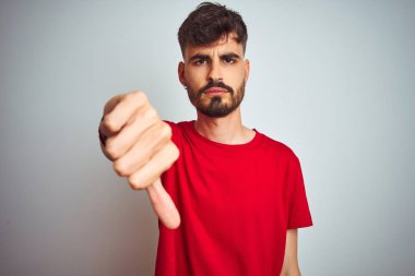 İzole edilmiş beyaz arka plan üzerinde duran kırmızı tişörtlü genç adam mutsuz ve kızgın görünüyor. Reddedilmiş ve olumsuz jestler yapıyor. Kötü ifade.