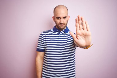 Sakallı, pembe izole edilmiş arka planda günlük çizgili mavi tişört giyen genç kel adam avucunun içi gibi şarkı söylemeyi kesiyor. Yüzünde olumsuz ve ciddi bir jest olan uyarı ifadesi.
