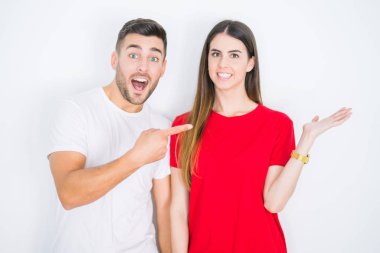 Genç ve güzel bir çift, beyaz izole edilmiş arka planda hayrete düşmüş ve kameraya gülümsüyor. Elleriyle ve parmaklarıyla gösteriyorlar..