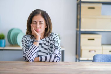 Orta yaş yaşlı kadın evde masada oturan yorgun görünümlü ve çapraz kolları ile depresyon sorunları ile sıkılmış düşünme.