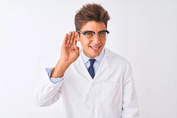 眼鏡をかけ 孤立した白い背景の上にコートを着た若いハンサムな科学者が 噂やゴシップに耳を傾けながら手で笑っている 病気の概念 — ストック写真