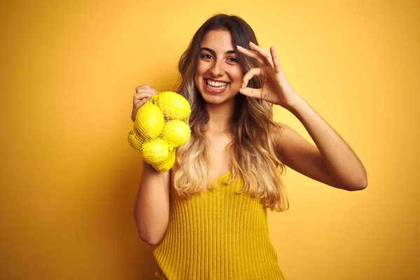 Mladá Krásná Žena Drží Síť Citronů Přes Žluté Izolované Pozadí — Stock fotografie