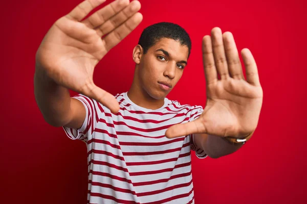 年轻英俊的阿拉伯男子 身穿条纹T恤 罩在孤立的红色背景上 用手心和手指头做框架 镜头透视 — 图库照片