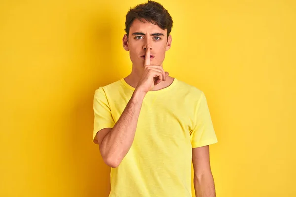 10代の少年は 孤立した背景の上に黄色のTシャツを着て唇に指で静かにするように求めている 沈黙と秘密の概念 — ストック写真