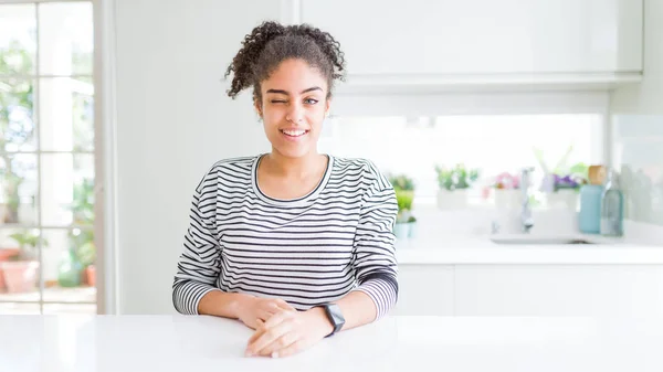 Beautiful african american woman with afro hair wearing casual striped sweater winking looking at the camera with sexy expression, cheerful and happy face.