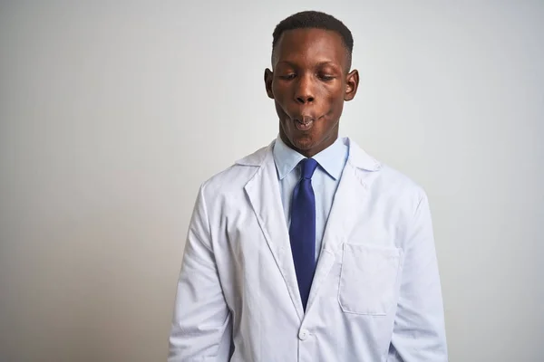 Young african american doctor man wearing coat standing over isolated white background making fish face with lips, crazy and comical gesture. Funny expression.