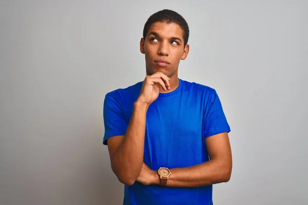 年轻英俊的Arab男子穿着蓝色的T恤站在孤立的白色背景之上 手放在下巴上思考问题 沉思的表情 脸上挂着沉思的笑容 怀疑的概念 — 图库照片