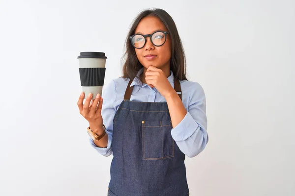 Young chinese barista woman wearing glasses holding coffee over isolated white background serious face thinking about question, very confused idea
