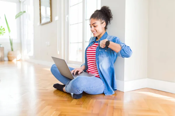 Young african american woman sitting on the floor using computer laptop with surprise face pointing finger to himself