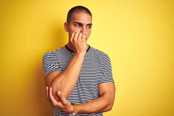 年轻的英俊男子穿着条纹T恤在黄色孤立的背景看起来紧张和紧张与手咬嘴指甲 焦虑问题 — 图库照片