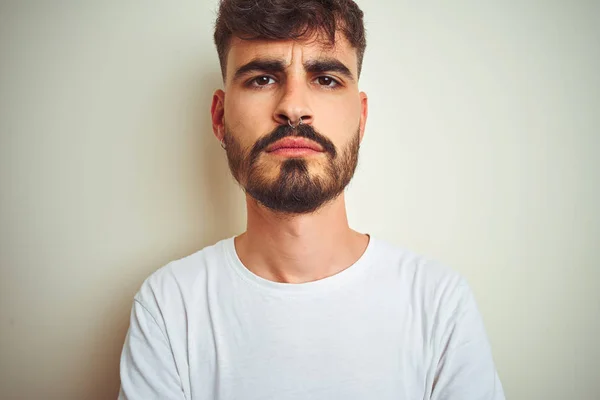 Young man with tattoo wearing t-shirt standing over isolated white background skeptic and nervous, disapproving expression on face with crossed arms. Negative person.