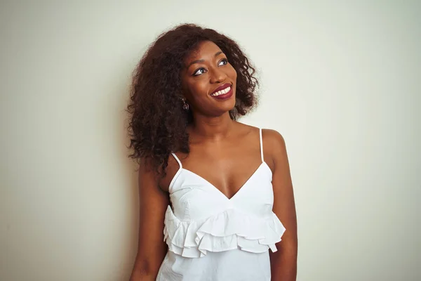 Young african american woman wearing t-shirt standing over isolated white background looking away to side with smile on face, natural expression. Laughing confident.