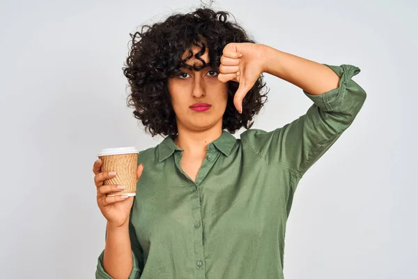 Young arab woman with curly hair drinking cup of coffee over isolated white background with angry face, negative sign showing dislike with thumbs down, rejection concept