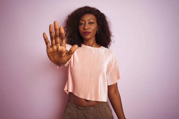 Young african american woman wearing t-shirt standing over isolated pink background doing stop sing with palm of the hand. Warning expression with negative and serious gesture on the face.