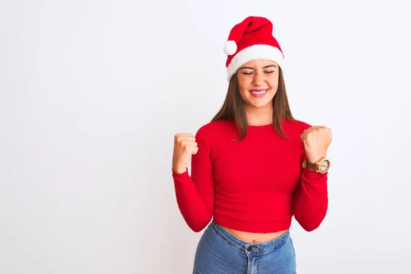 孤立した白い背景の上に立ってクリスマスサンタの帽子を身に着けている若い美しい女の子は非常に幸せと腕を上げて勝者のジェスチャーを行う興奮し 笑顔と成功のために叫んでいます お祝いのコンセプト — ストック写真