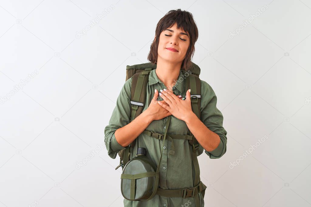 Beautiful hiker woman wearing backpack and water canteen over isolated white background smiling with hands on chest with closed eyes and grateful gesture on face. Health concept.