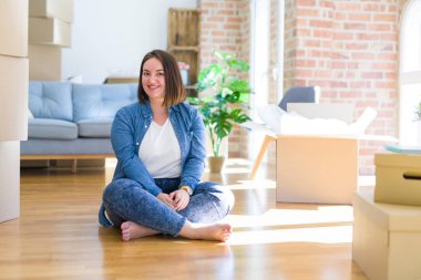 Genç ve cüsseli bir kadın karton kutuların etrafında oturmuş yüzünde mutlu ve havalı bir gülümsemeyle yeni bir eve taşınıyor. Şanslı kişi..