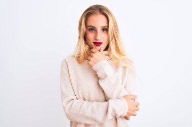 Balıkçı yaka kazak giyen genç ve güzel bir kadın izole edilmiş beyaz arka plan üzerinde duruyor kameraya kollarını kavuşturup gülümseyerek ve çenesini kaldırarak bakıyor. Olumlu düşünüyorum..